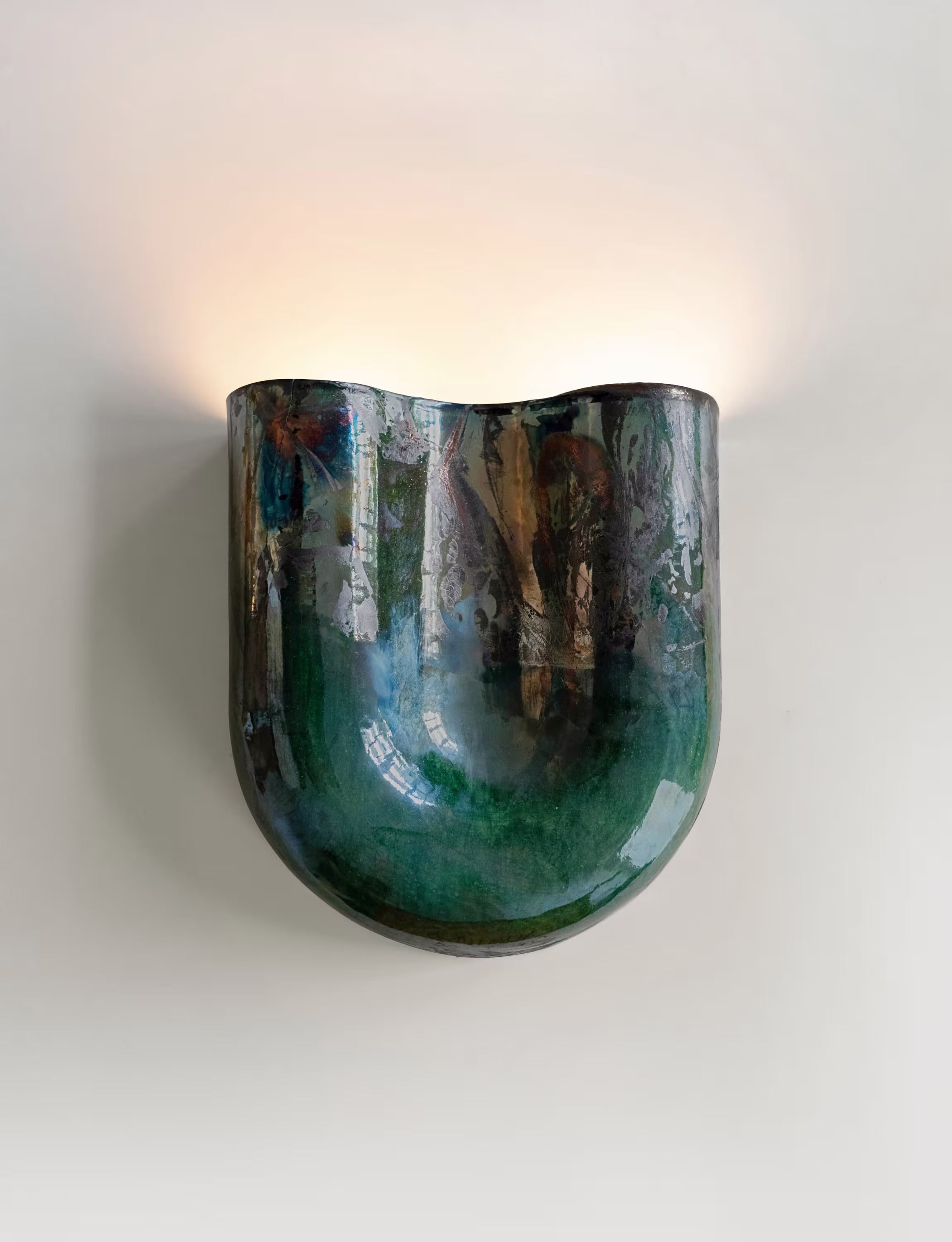 Wall-mounted copper sconce with wavy shape and raku finish, casting warm light against a plain background.