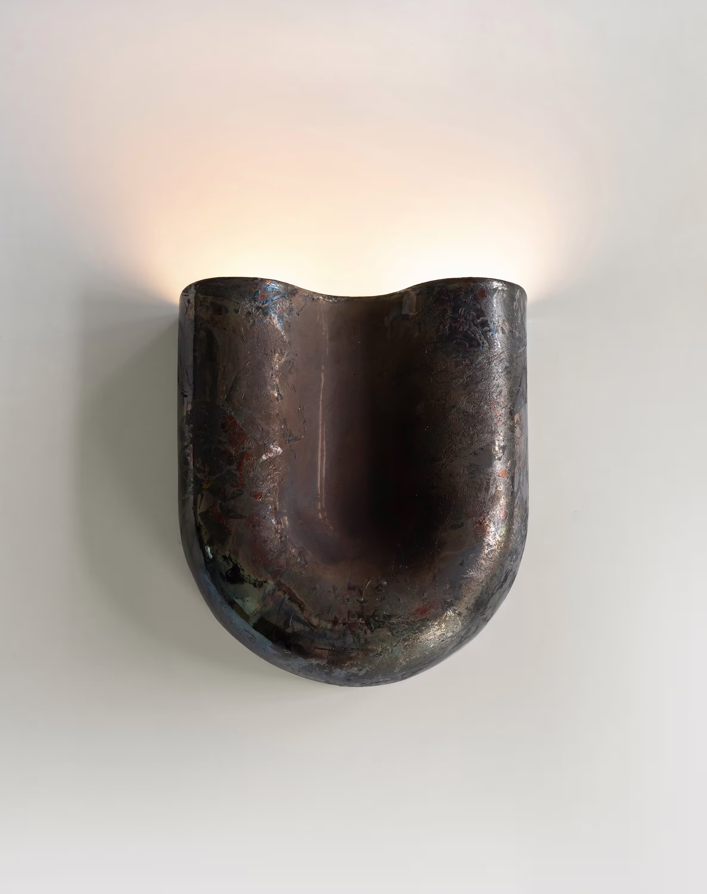Copper sconce with a wavy, textured finish, mounted on a white wall, glowing with upward light.