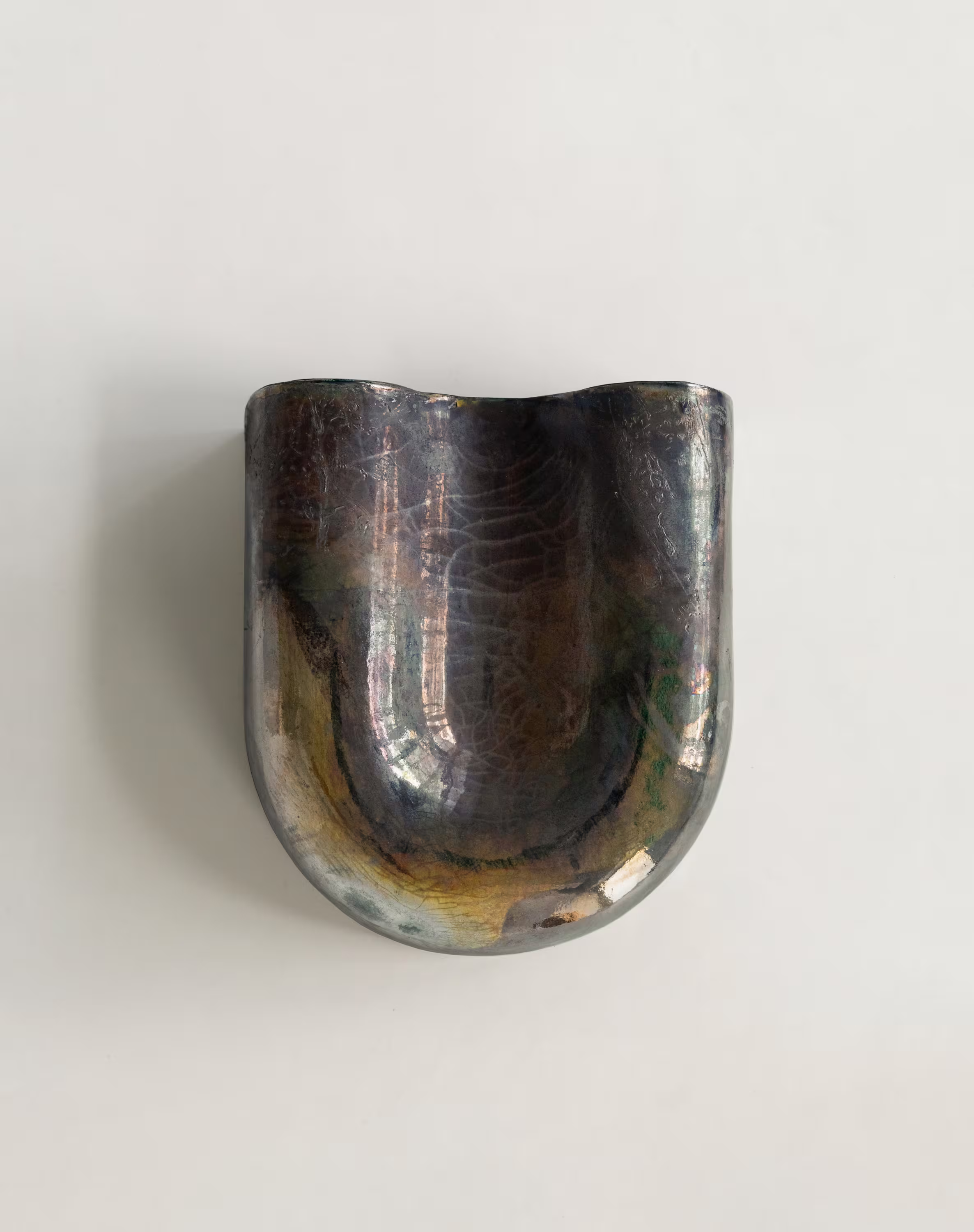 Copper sconce with a glossy, raku finish displaying iridescent colors and subtle crackle patterns, mounted on a plain white wall.